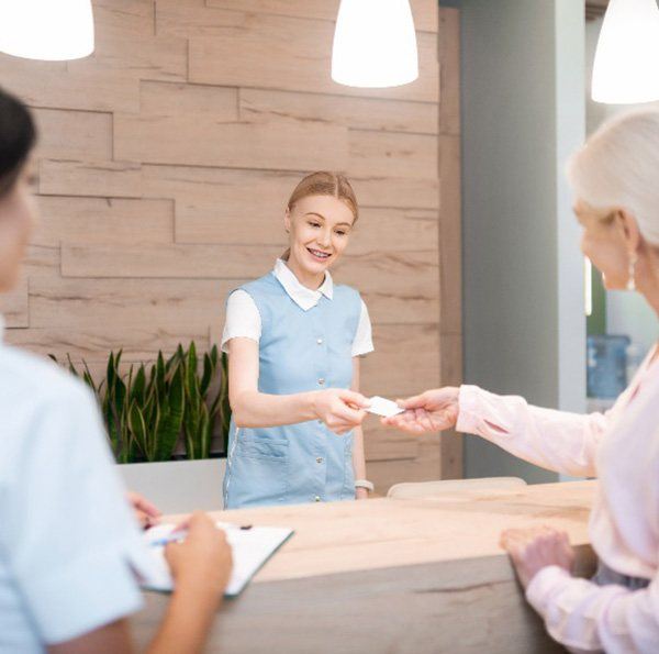 Woman smiling while handing dental receptionist credit card