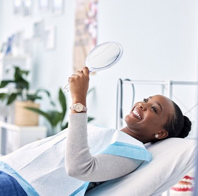 Woman smiling at reflection in handheld mirror