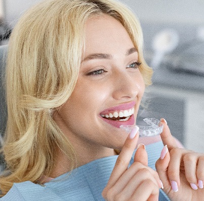 Blonde woman in dental chair about to put in Invisalign aligner