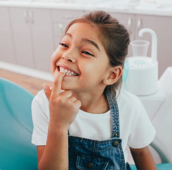 Little girl pointing to smile during children's dentistry visit