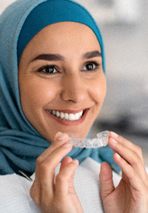 Woman with blue headwrap smiling about to insert Invisalign