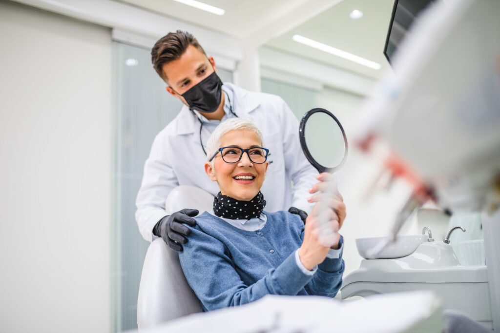 Dentist looking over woman's shoulder as she admires treatment results